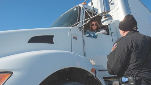 Commercial vehicle stopped roadside while a law enforcement officer speaks with the driver during a truck inspection.
